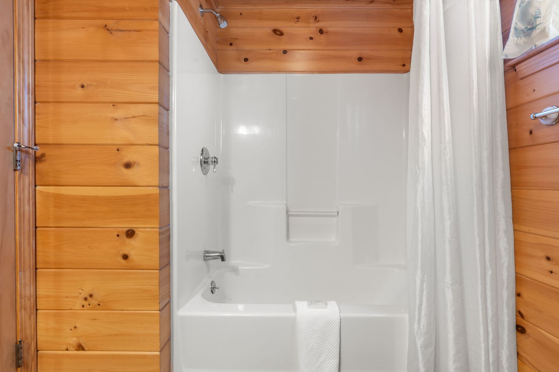 White shower in a wood-paneled bathroom. White curtain, towel, and fixtures.