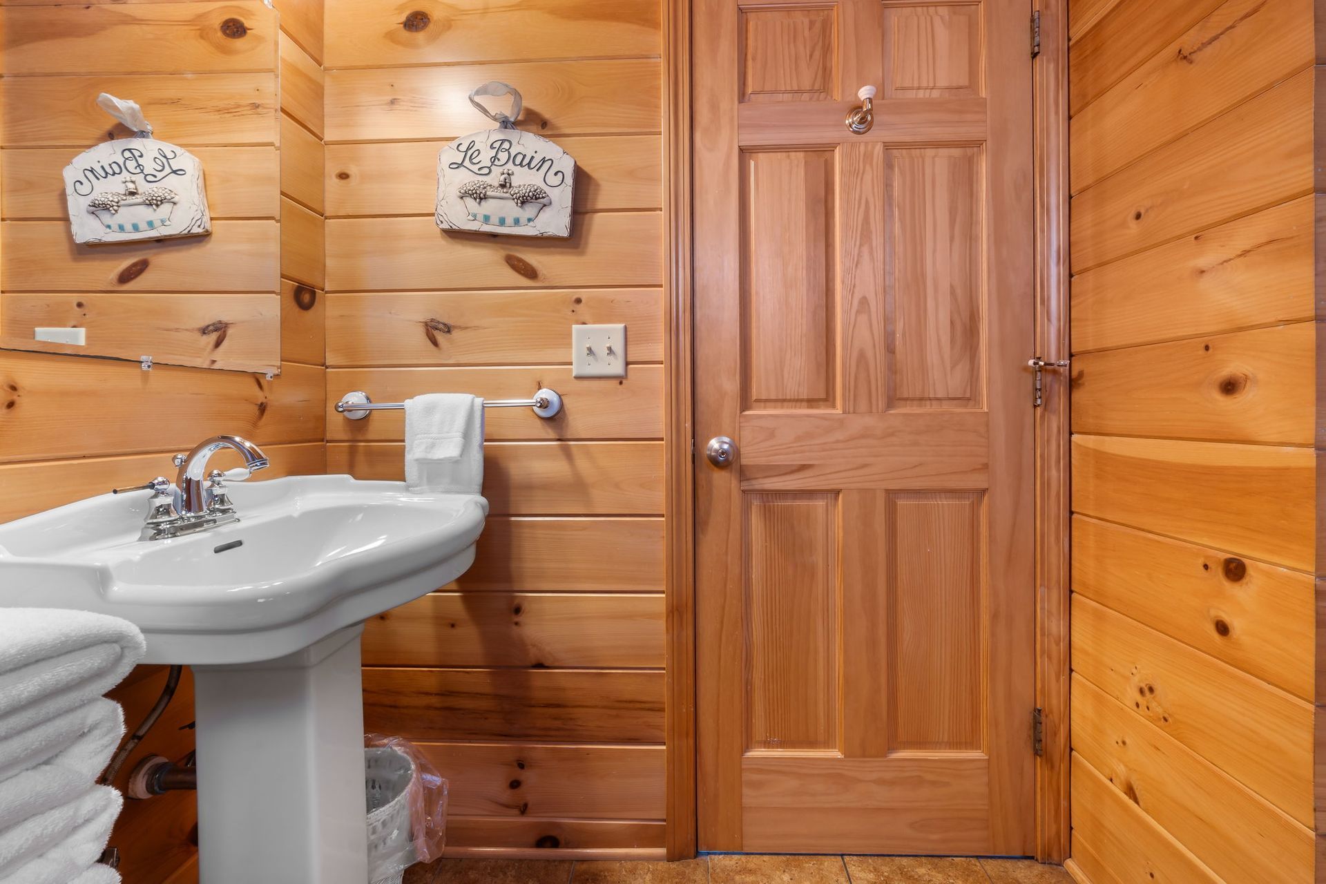 Bathroom with wooden paneling, pedestal sink, door, and decorative wall art.