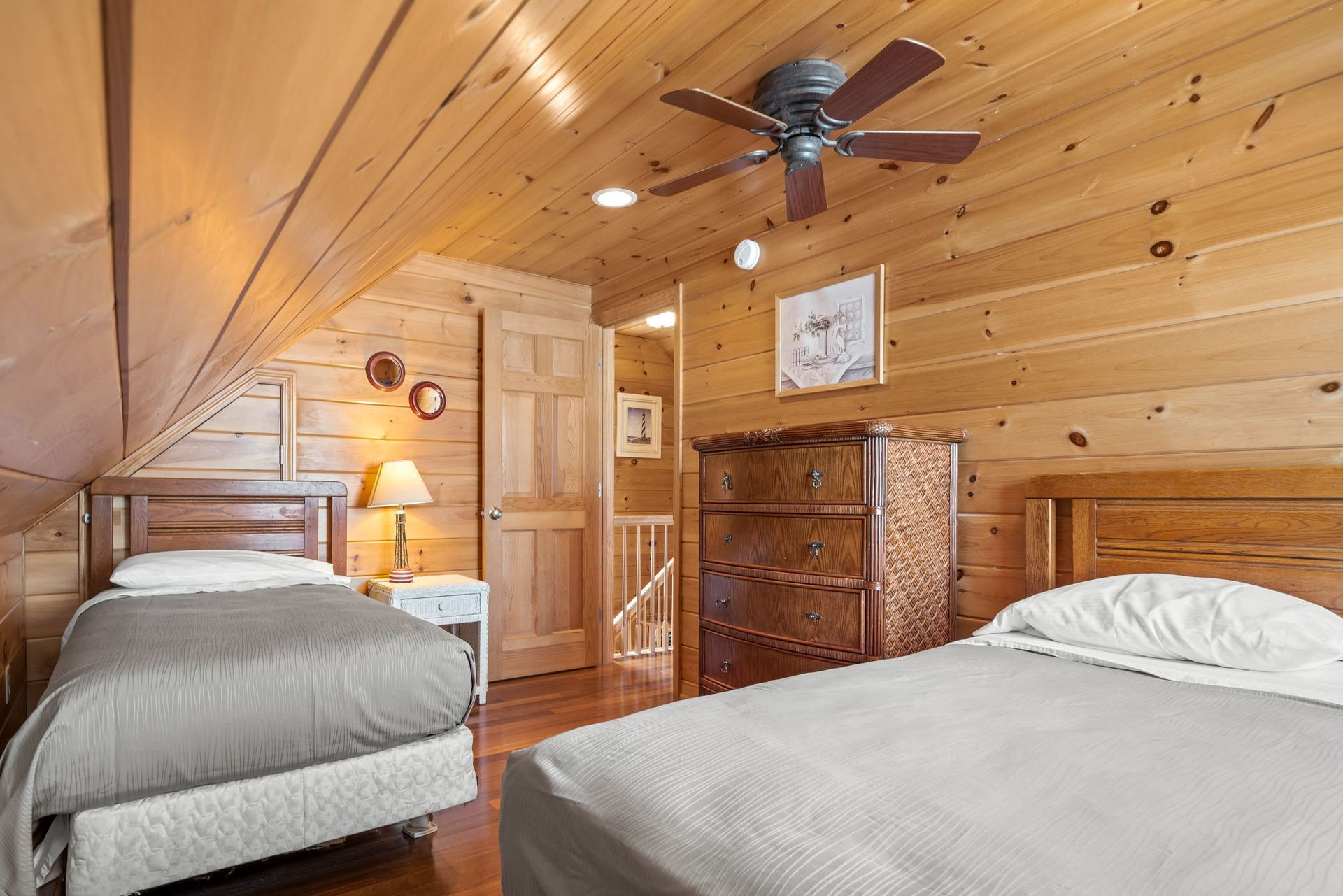 Bedroom with two beds, wood paneling, dresser, and ceiling fan.