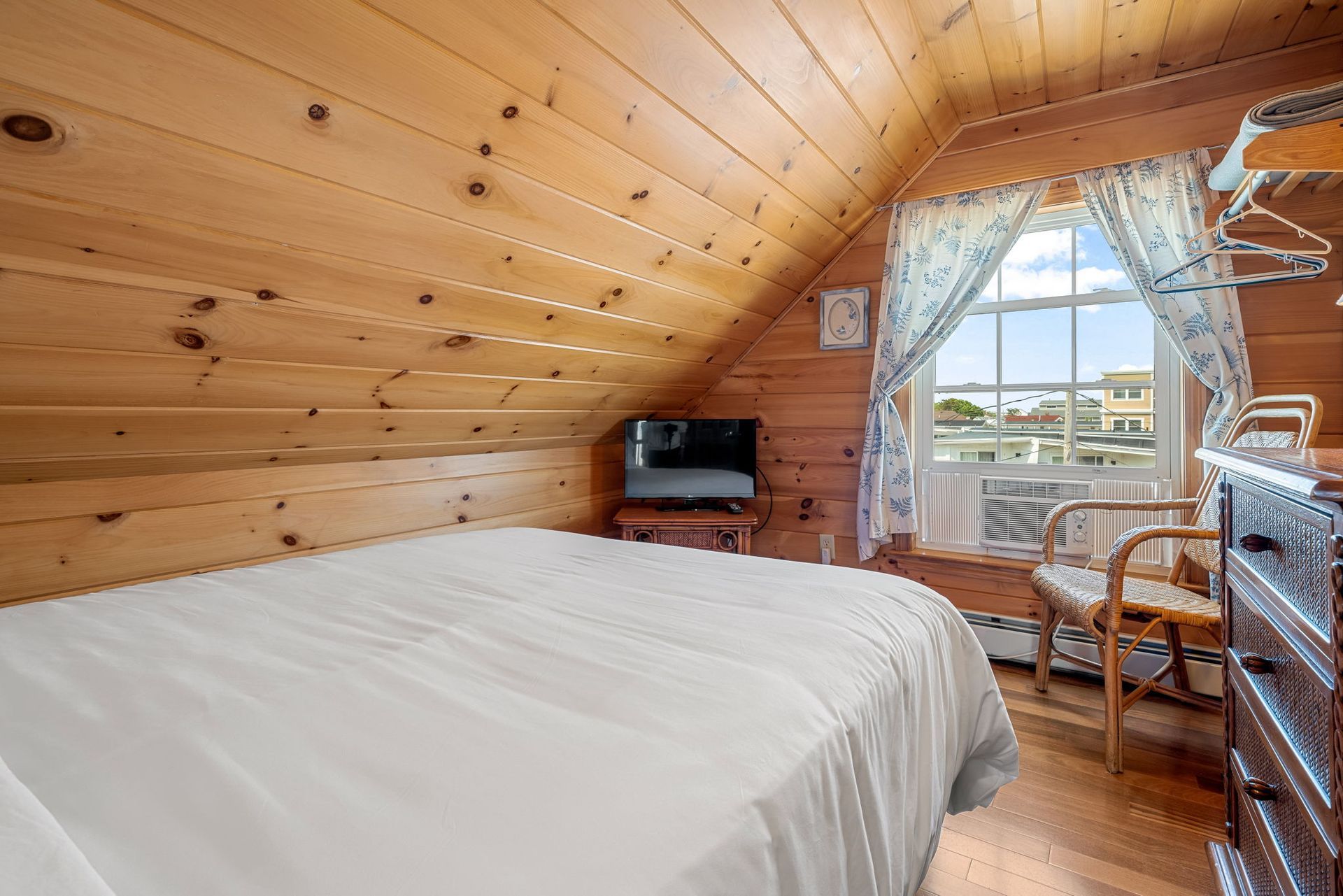 Bedroom with wooden walls, bed, TV, window with curtains, and a chair.