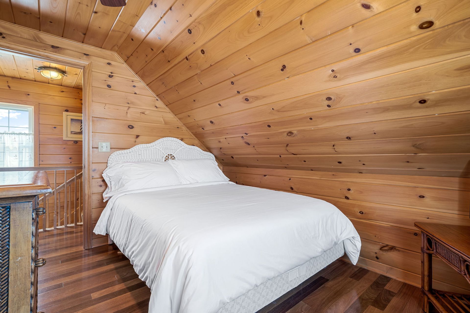Cozy bedroom with wooden walls, a bed with white linens, and a small window on the left.