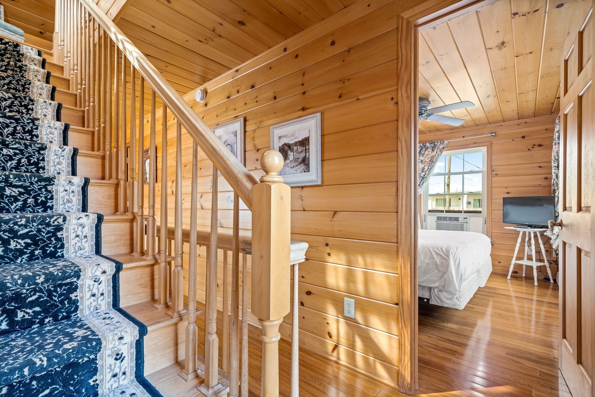 Wooden staircase leading to bedroom with bed. Wood paneling and blue carpet.