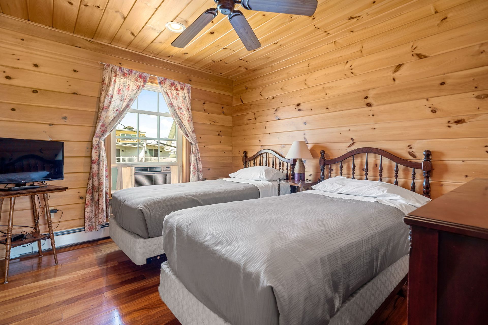 Bedroom with two twin beds, wood paneling, floral curtains, and a ceiling fan.