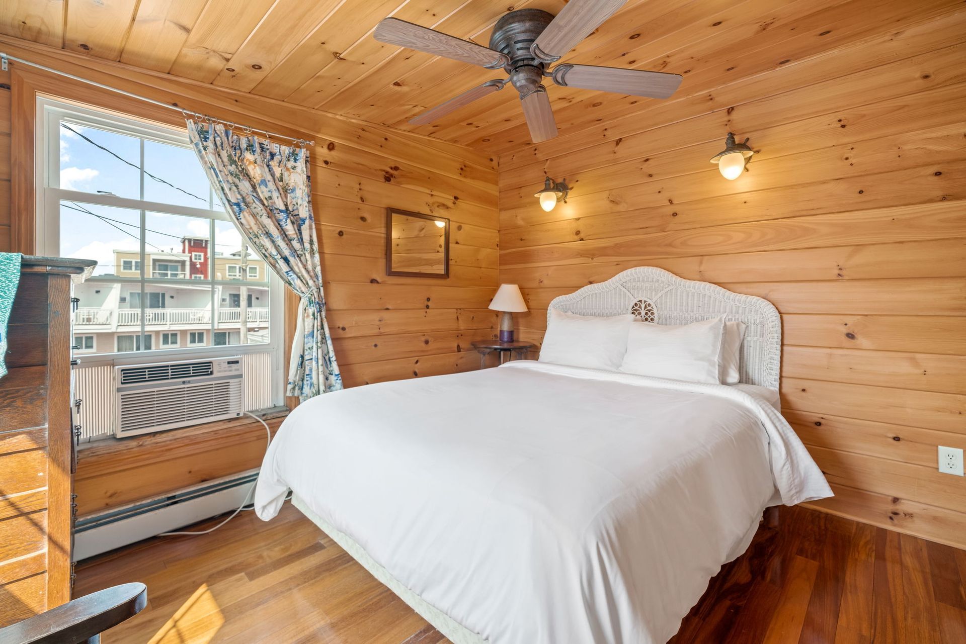 Cozy bedroom with wood paneling, a white bed, and a window overlooking a building.