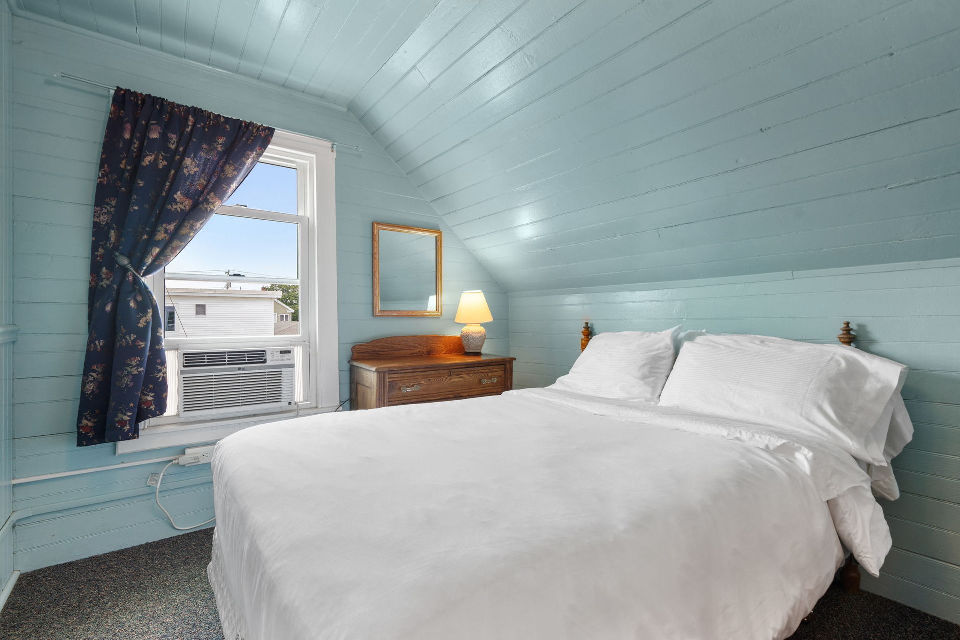 Bedroom with blue walls, a white bed, and a window with a dark curtain.