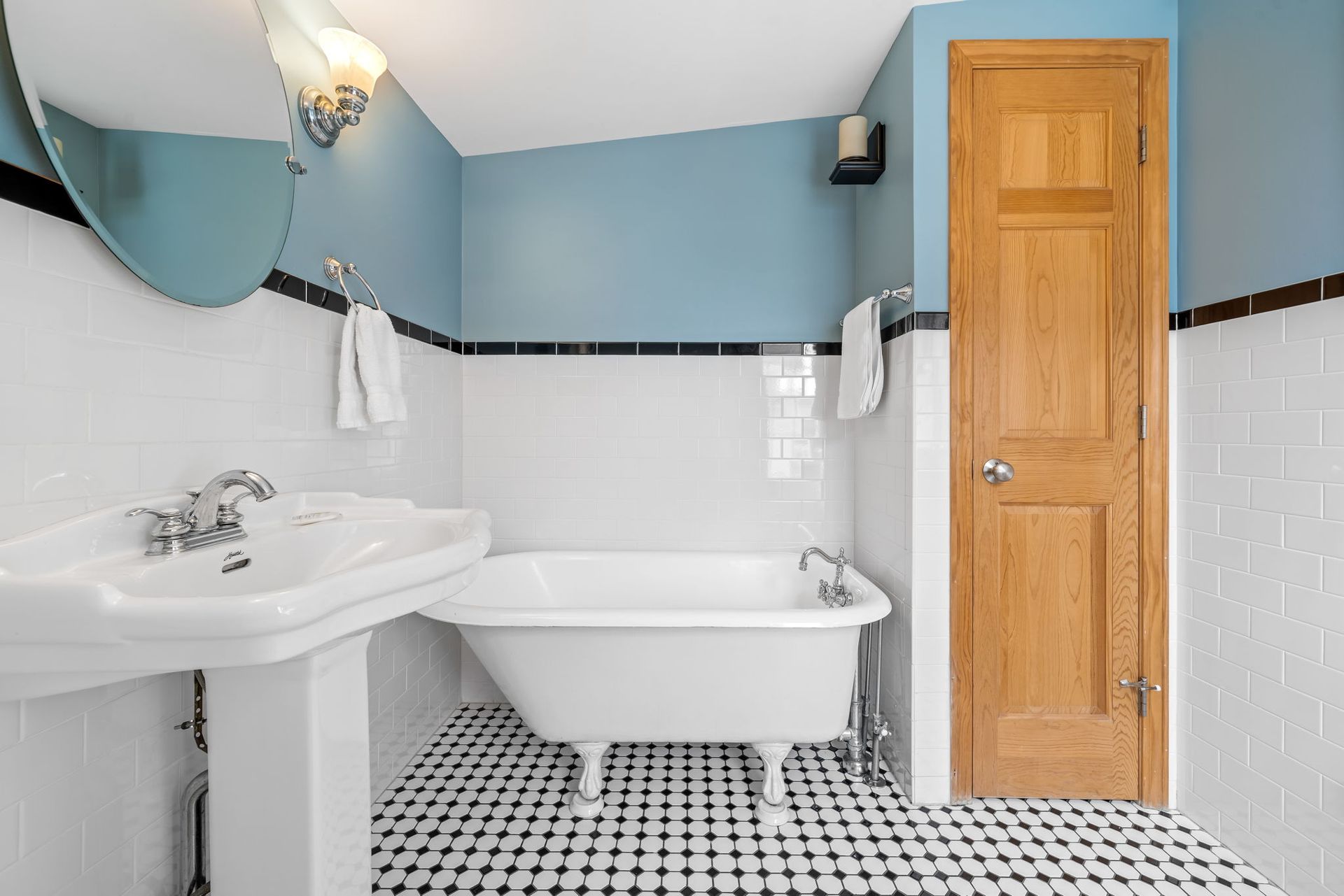 Bathroom with blue walls, white fixtures, black and white tile floor, and a wooden cabinet.