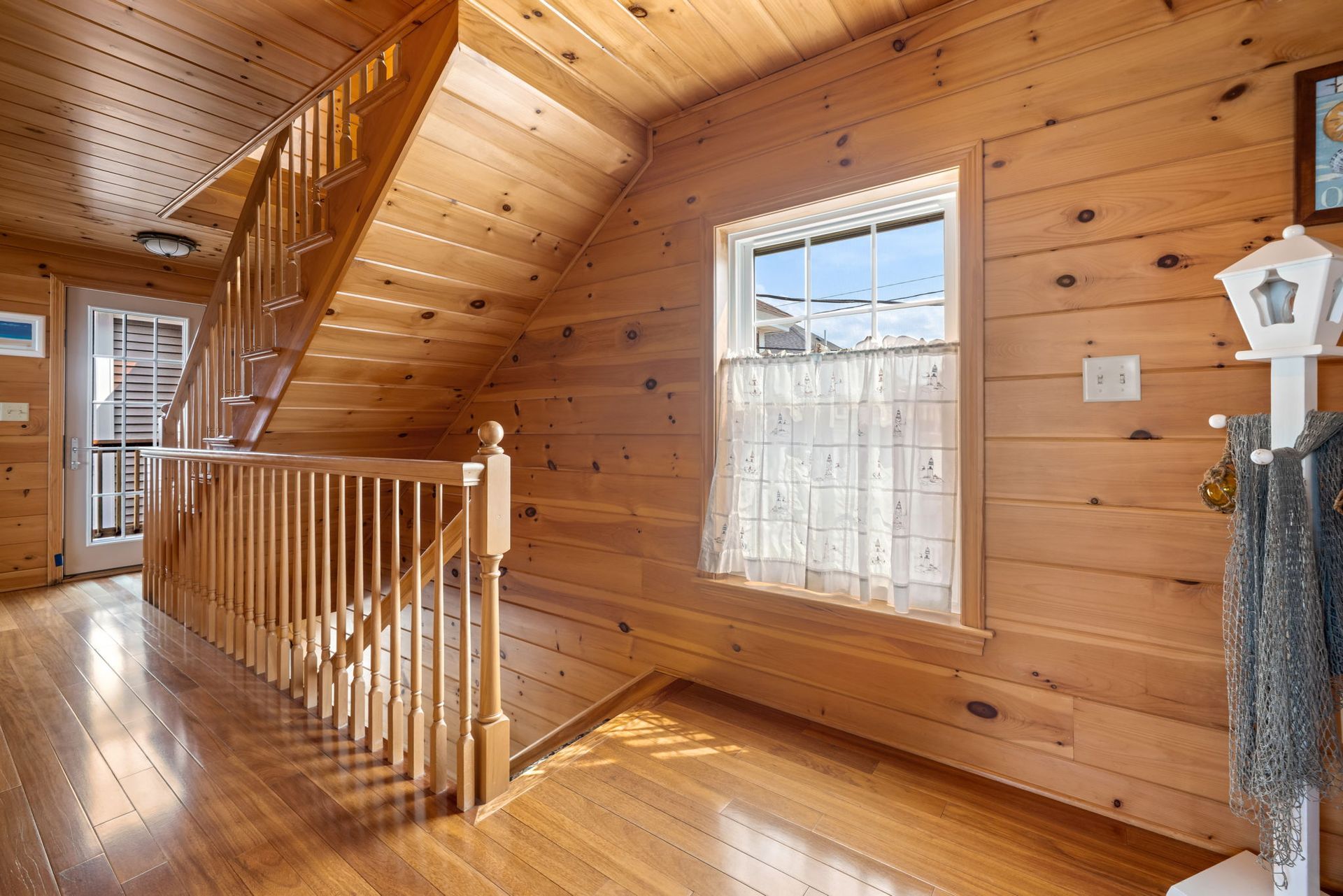 Wooden-paneled hallway with stairs, window, and railing; a decorative post holds a net.