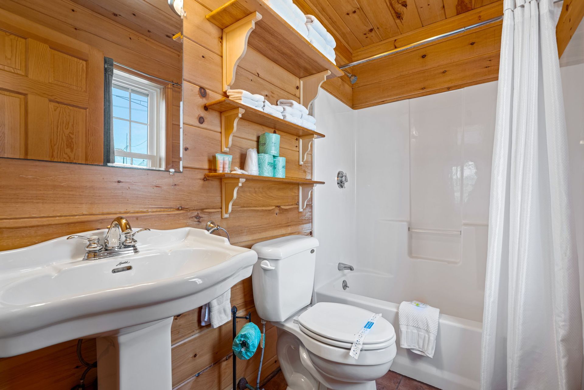 Bathroom with wooden walls, white fixtures, and a shower.
