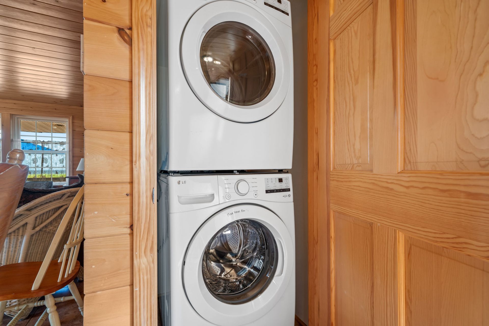 Stacked white washer and dryer units, in a wooden paneled alcove.