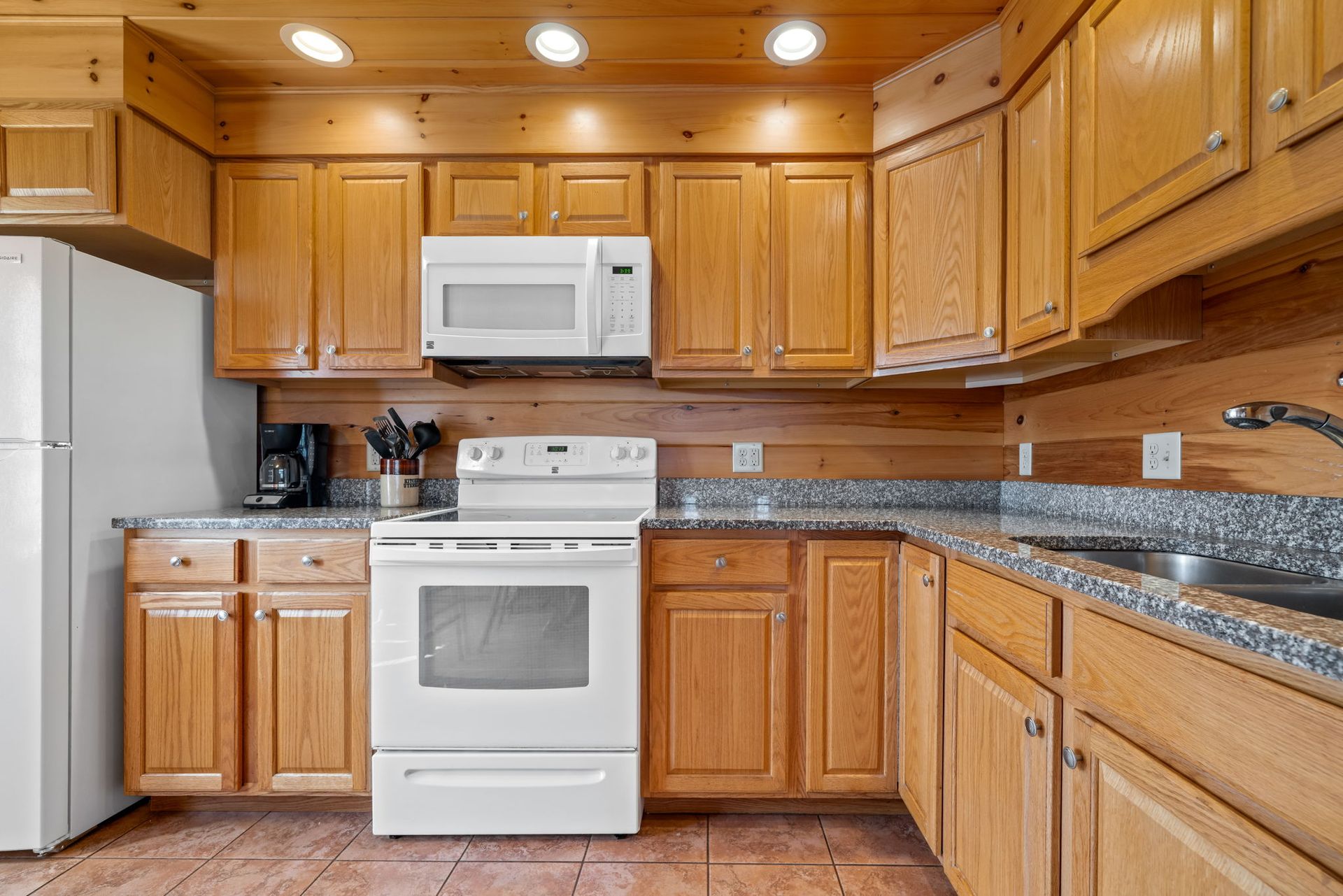 Kitchen with light wood cabinets, white appliances, and gray countertops.