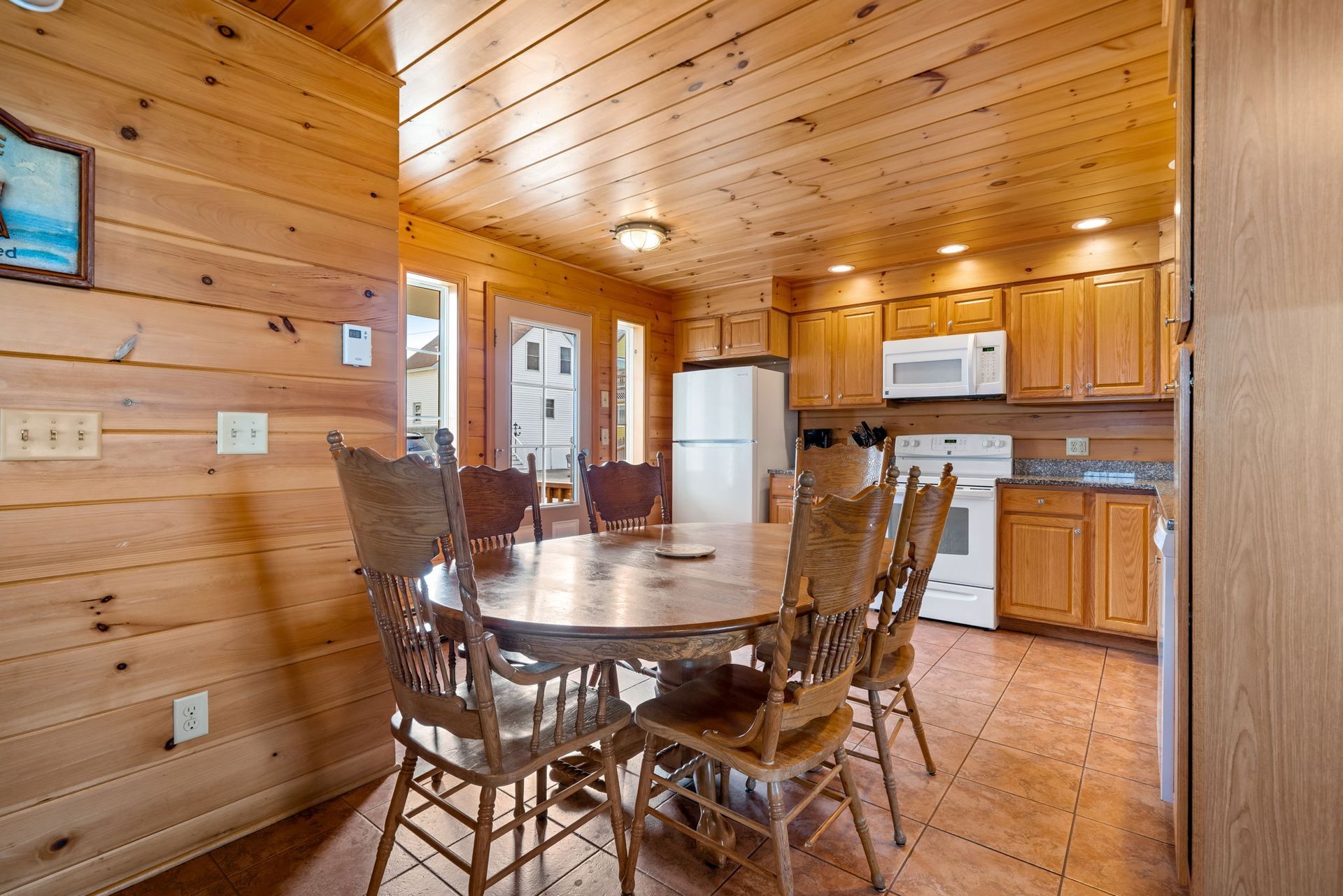 Dining area with wooden table, chairs, and kitchen in a cabin-like setting.