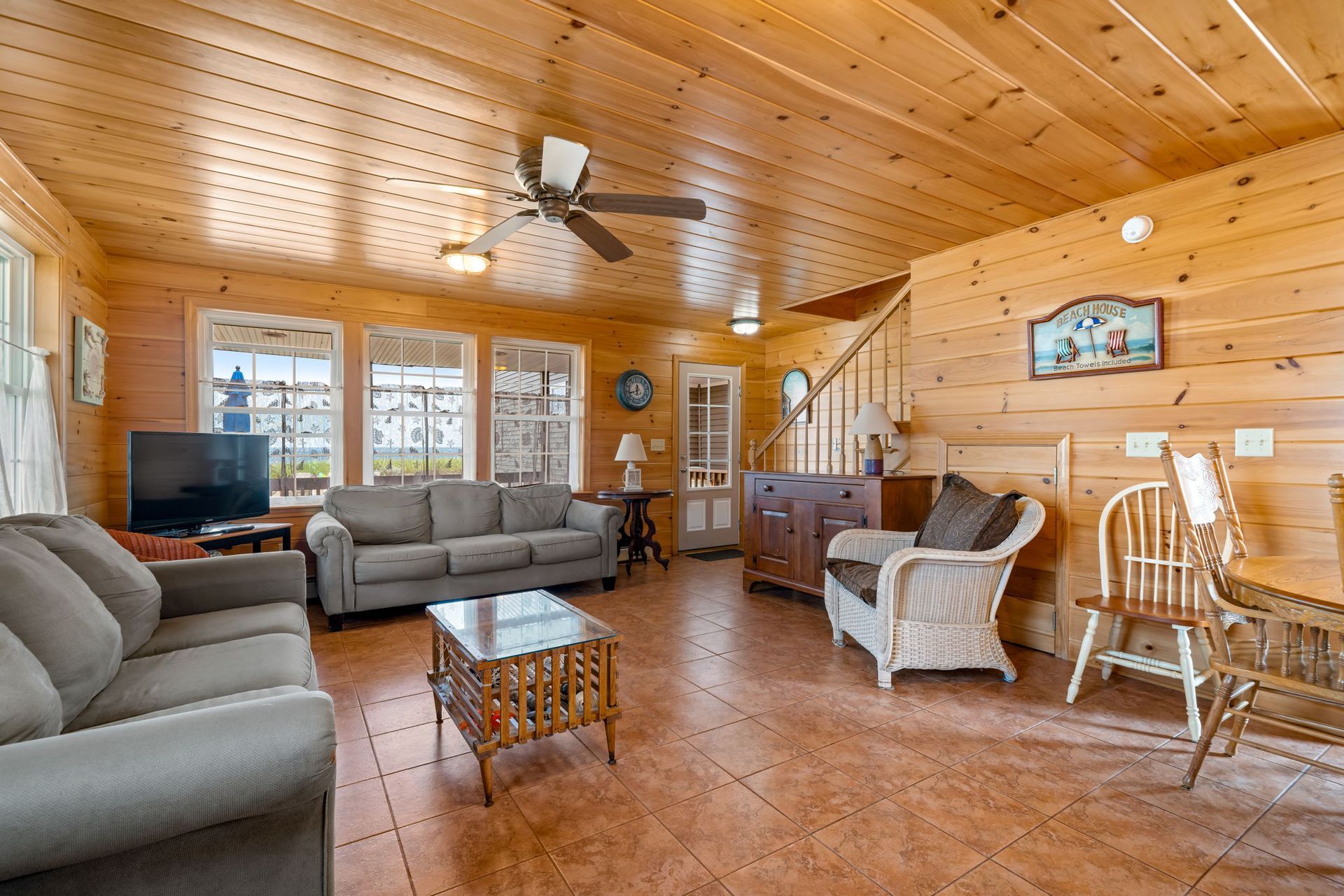Cozy living room with wood paneling, couches, and a dining area.
