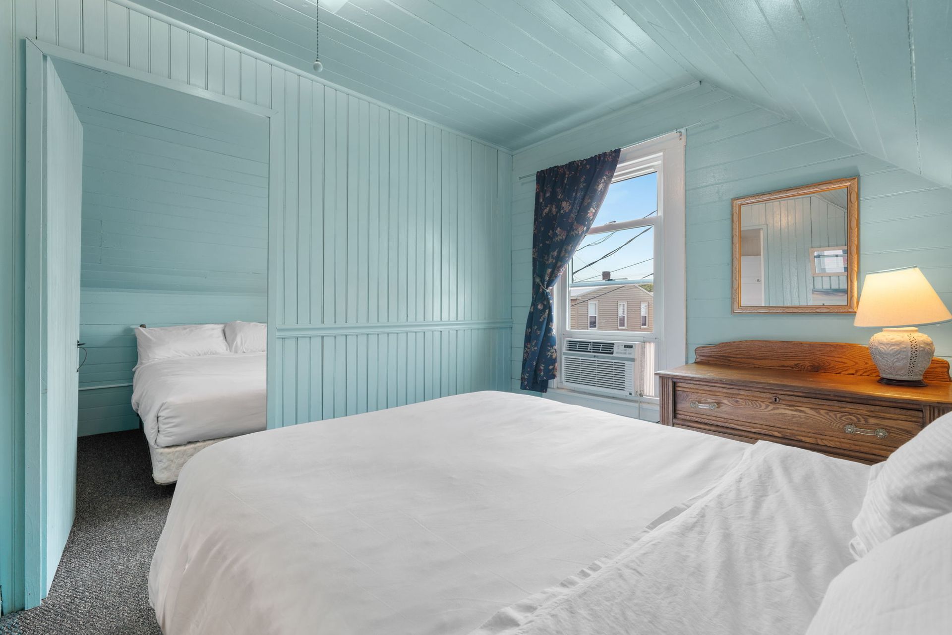 Bedroom with light blue walls, a white bed, and a view out a window.