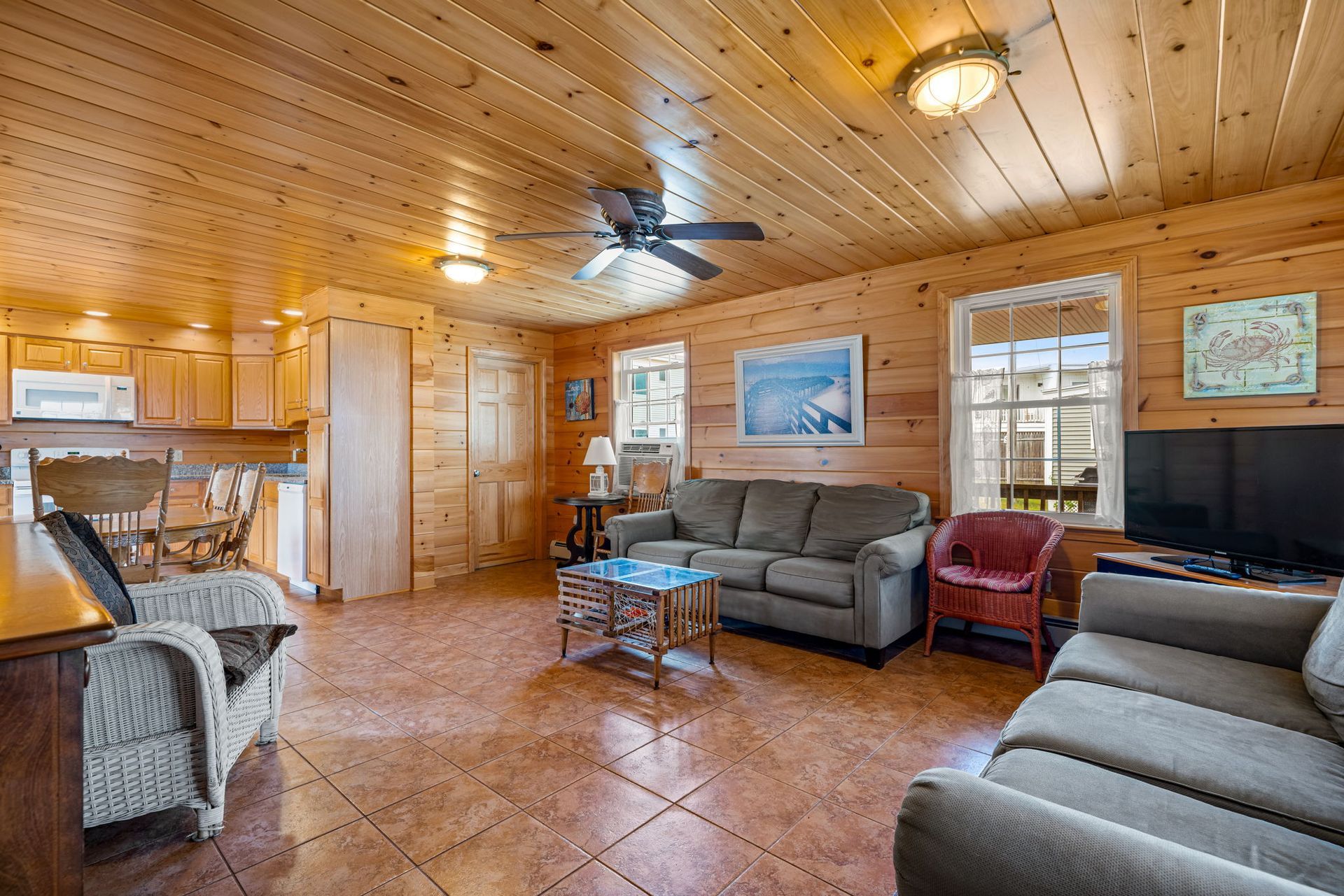 Cozy living room with wood paneling, two couches, kitchen, and windows.