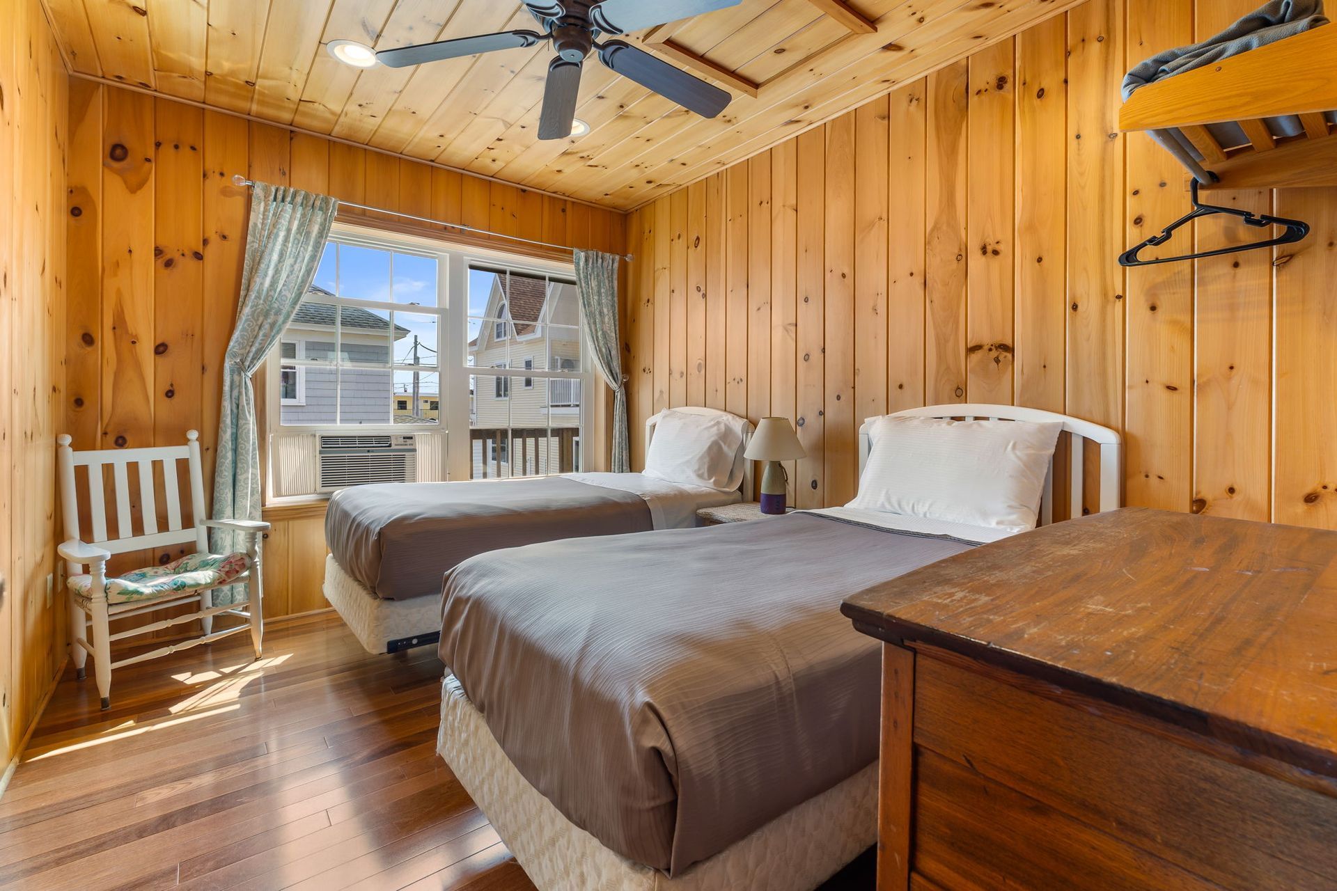 Bedroom with two twin beds, wooden walls, window, and ceiling fan.