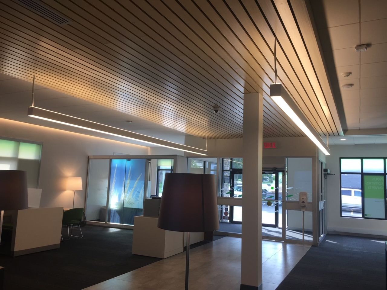 Un hall d'entrée moderne avec un plafond en bois perforé, un éclairage encastré et une porte d'entrée en verre.
