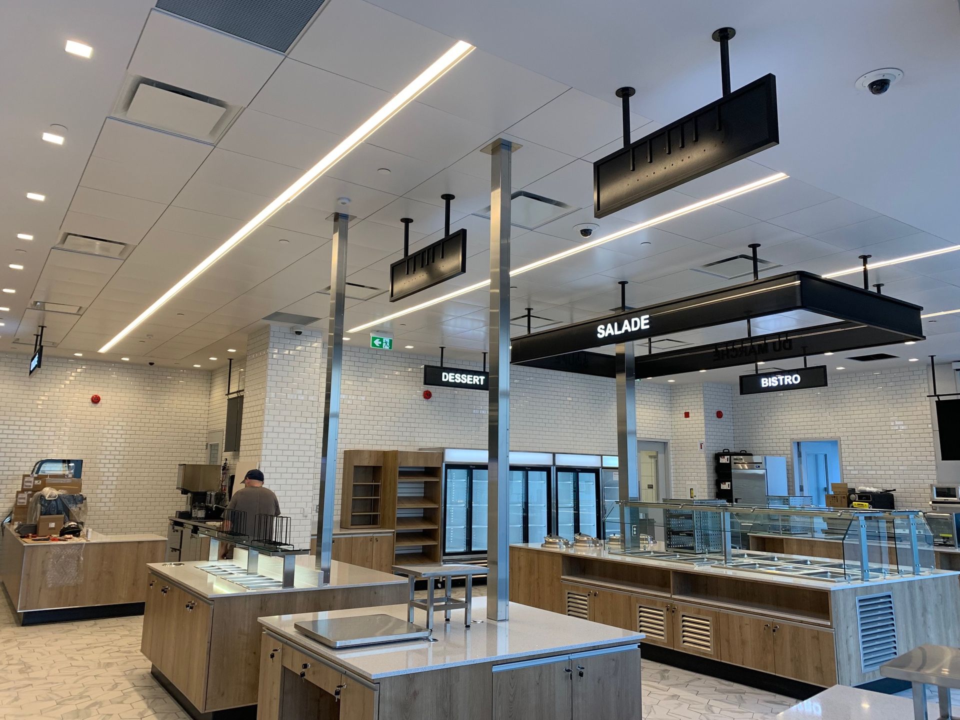 Cuisine commerciale bien éclairée avec divers postes de restauration, signalisation et un client à la fois.