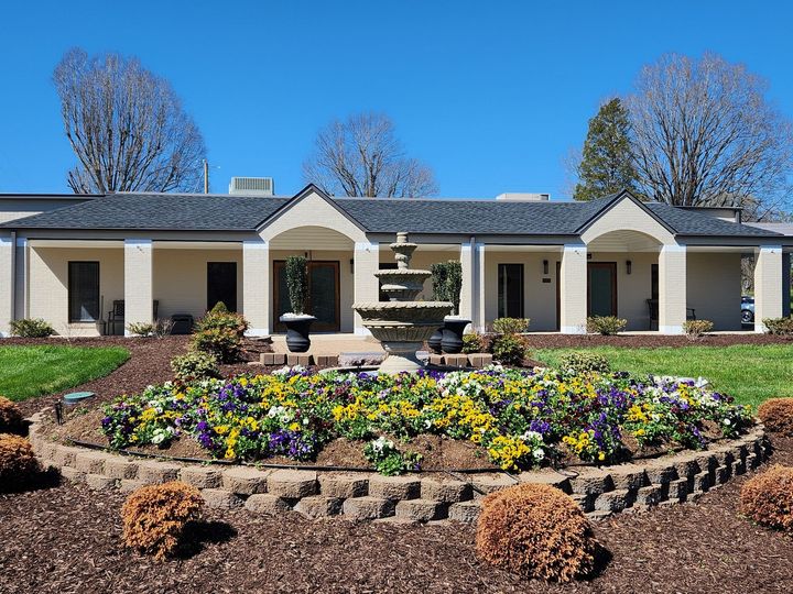 Single-story house with a landscaped front garden and a colorful flower bed under a bright blue sky