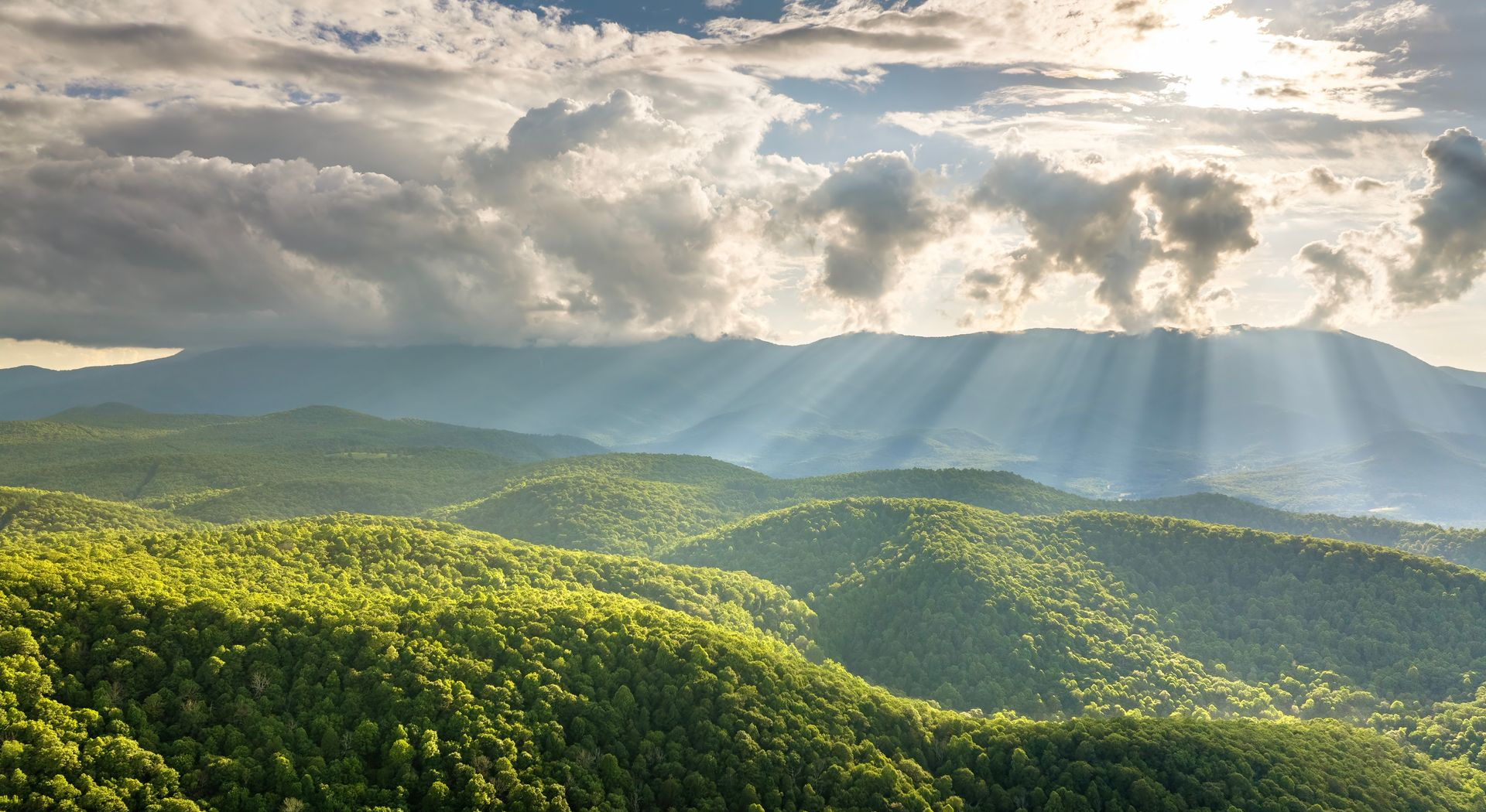 Sunlit green hills under dramatic clouds with beams of sunlight breaking through
