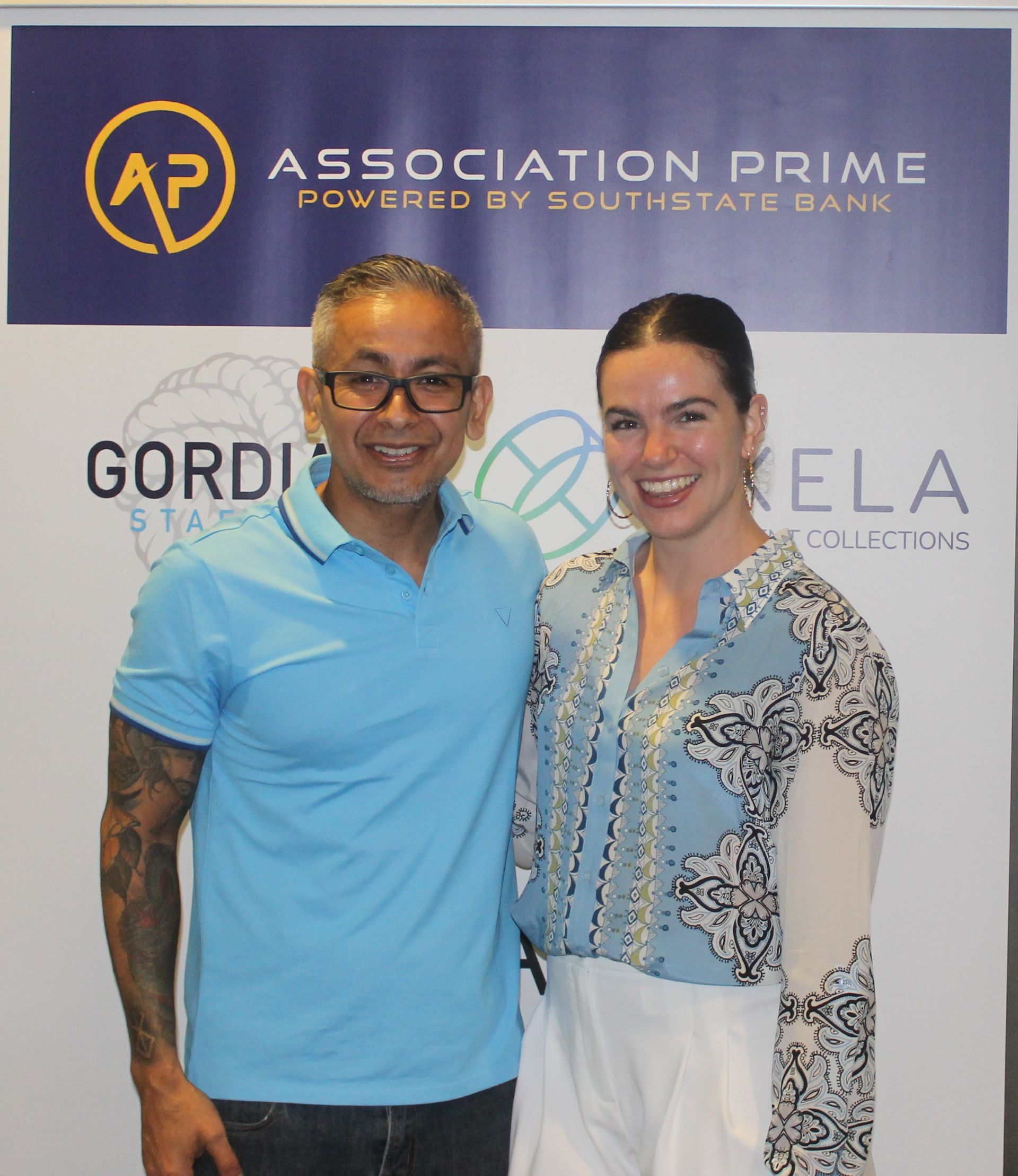 A man and a woman are posing for a picture in front of a banner that says association prime