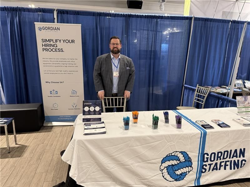 A man is standing in front of a gordian staffing table.