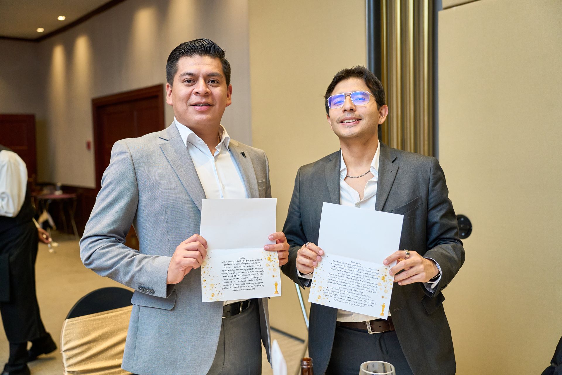 Two men in suits are standing next to each other holding papers.