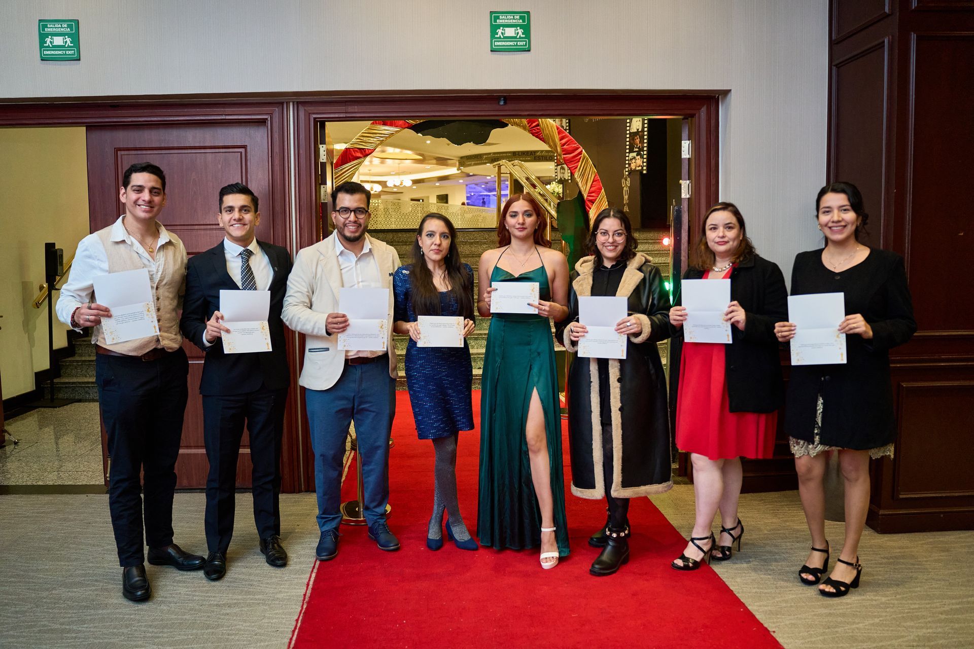 A group of people standing on a red carpet holding papers.