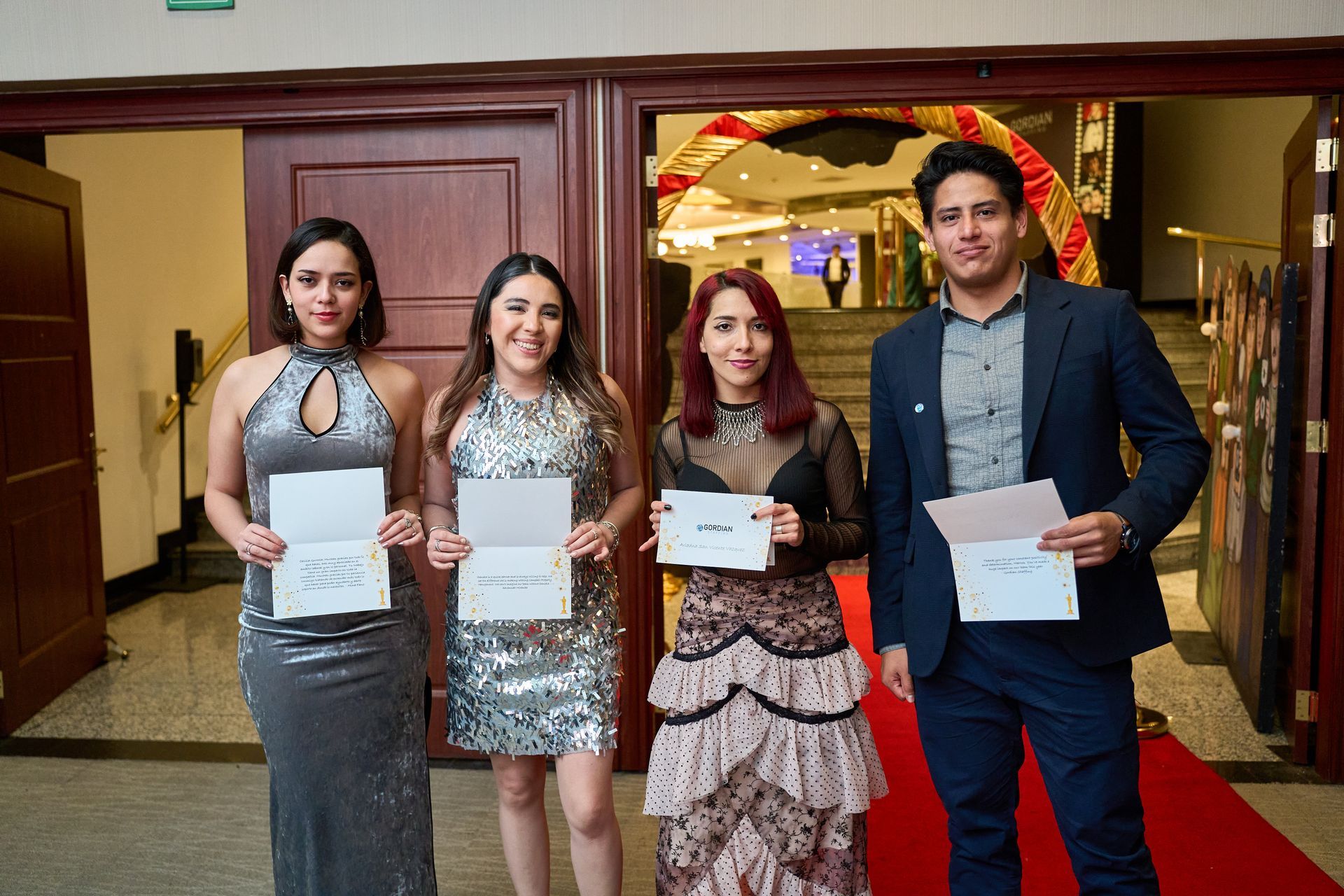 A group of people are standing on a red carpet holding papers.
