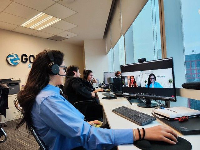 A woman wearing headphones is sitting at a desk in front of a computer monitor.
