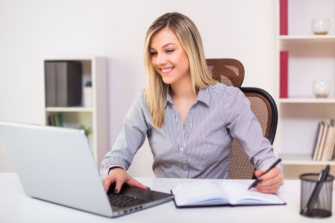 A woman is sitting at a desk using a laptop computer.