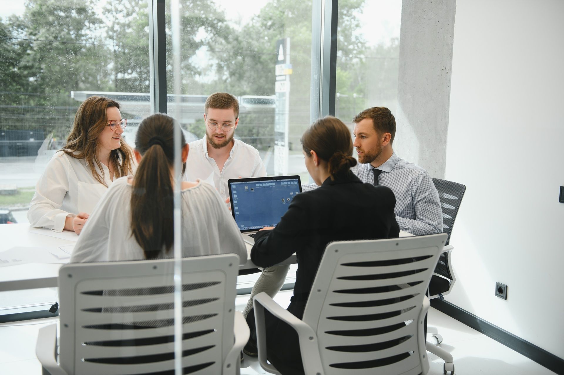 A group of people are sitting around a table with a laptop.