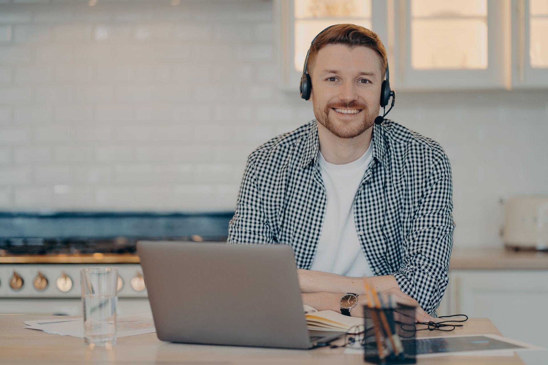 A man wearing headphones is sitting at a desk in front of a laptop computer.