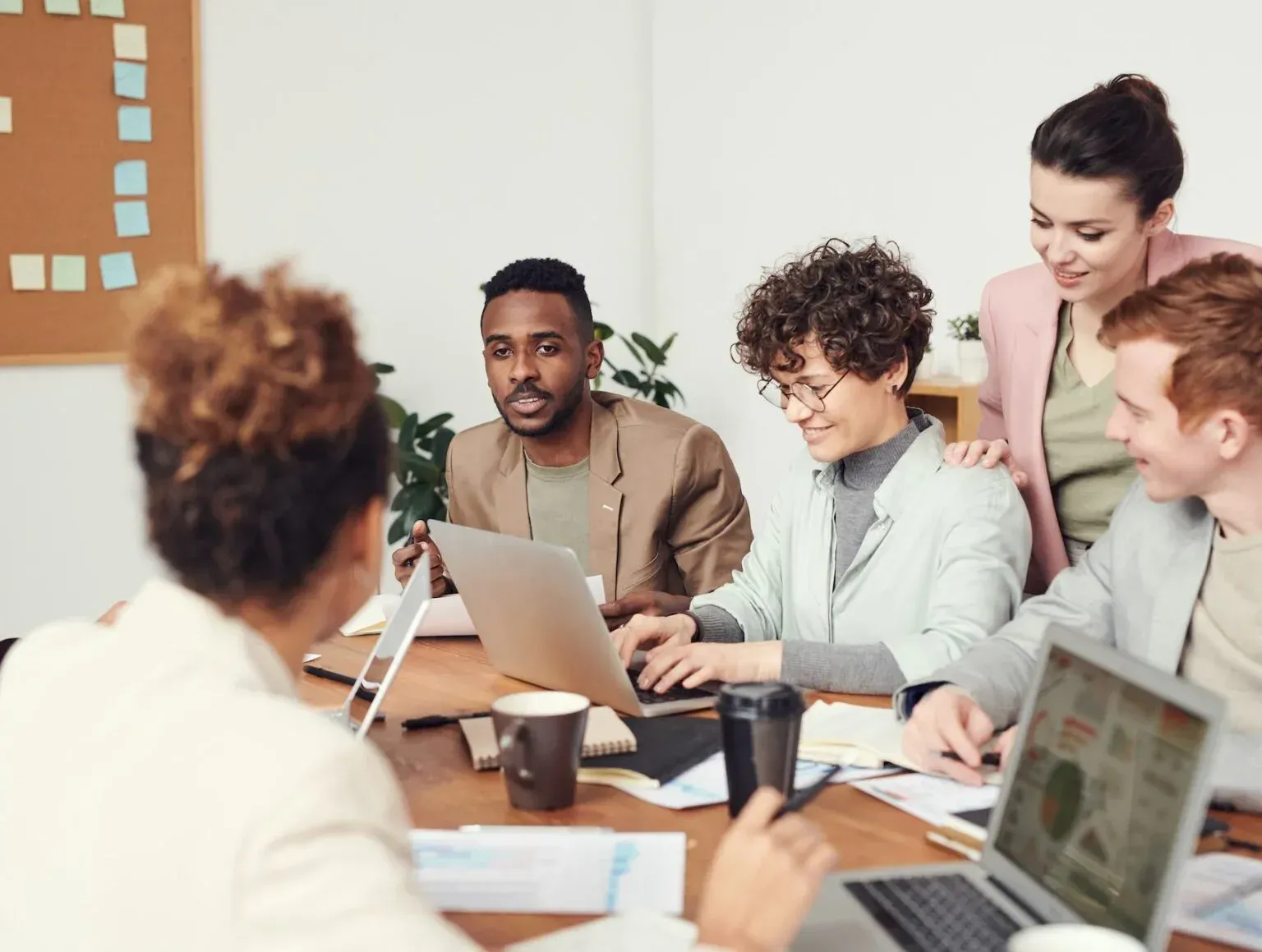 A group of people are sitting around a table with laptops.