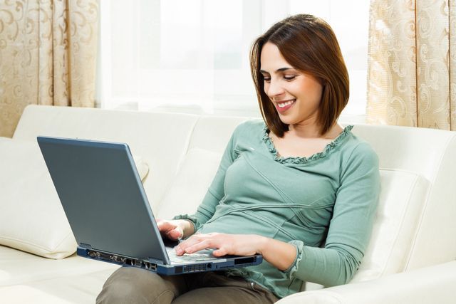 A woman is sitting on a couch using a laptop computer.