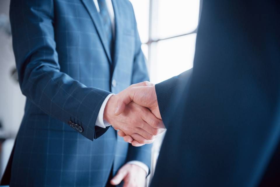Two men in suits are shaking hands in an office.