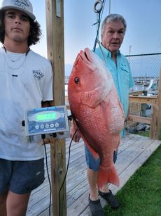 Two men are standing next to each other holding a large red fish.
