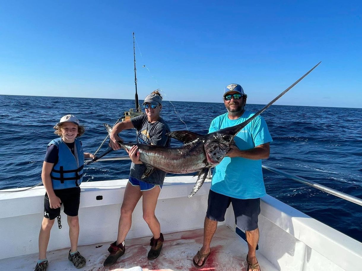 A man and two children are standing on a boat holding a large fish.