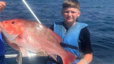A young boy is holding a large red fish on a boat.