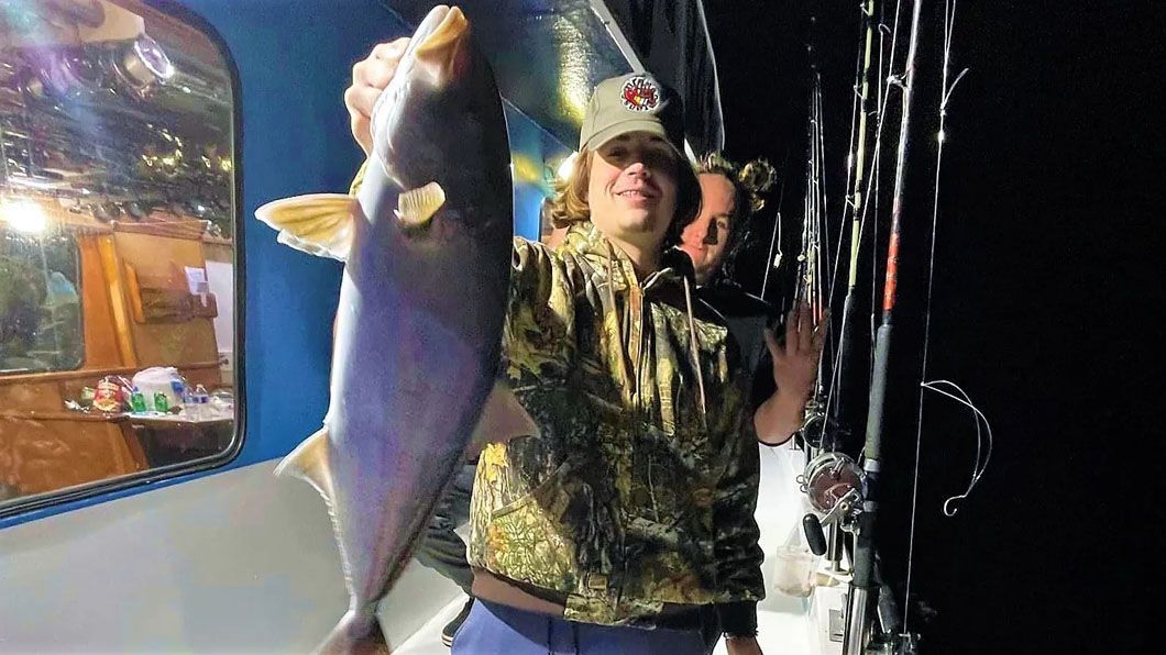 A man is holding a large fish in his hands on a boat.