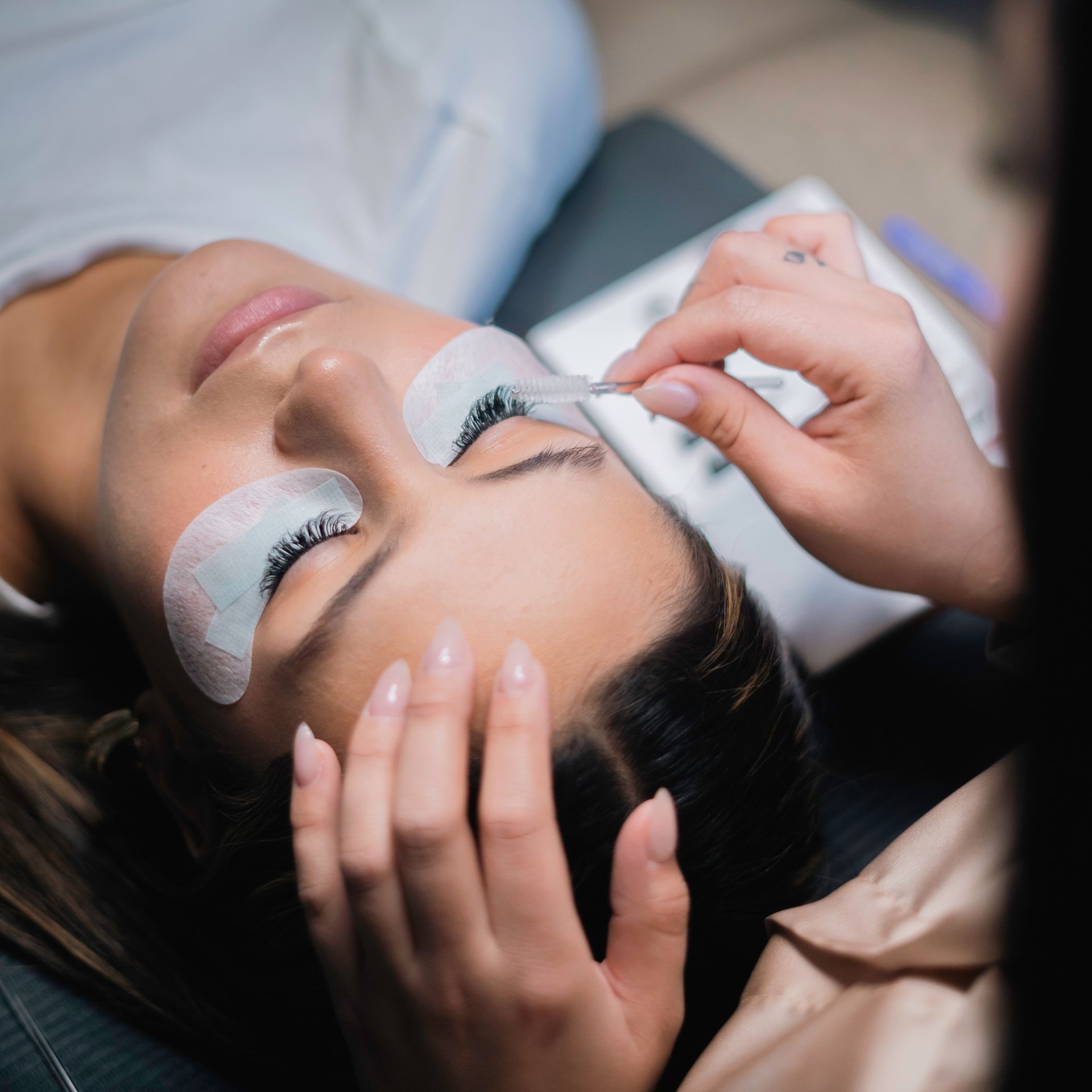 A woman with green nails is applying mascara to her eyebrows.