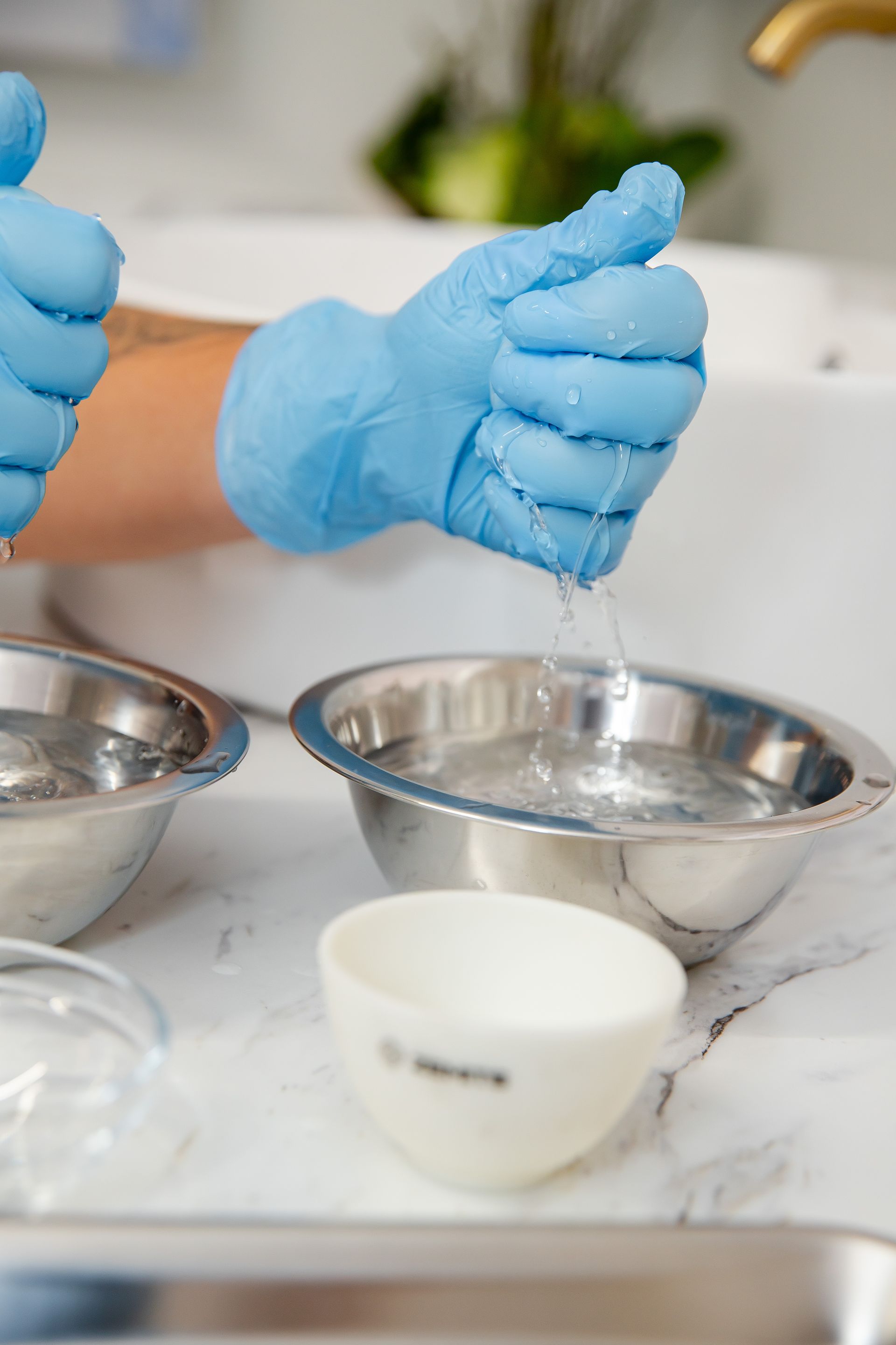 A person wearing blue gloves is pouring water into a metal bowl.