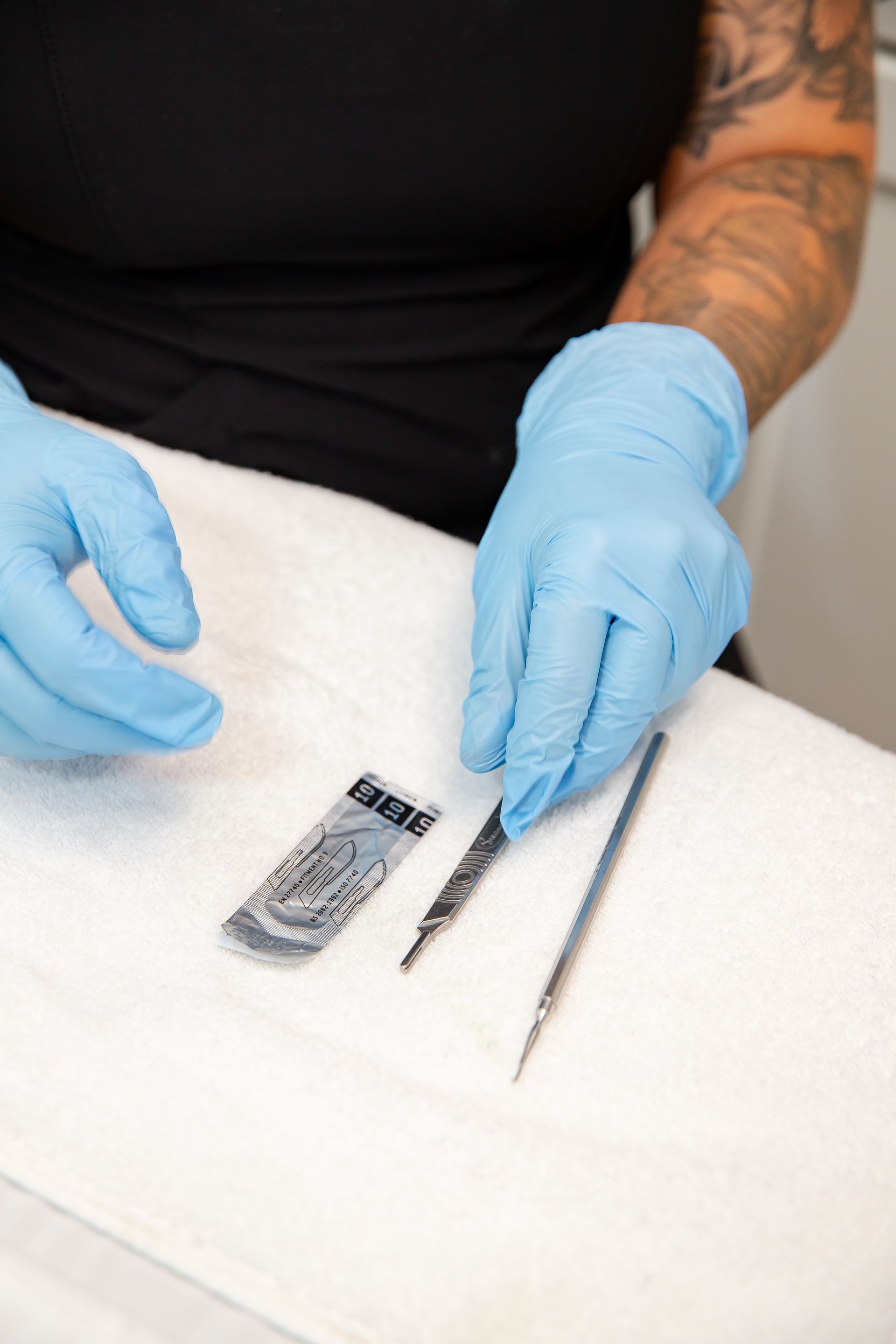 A person wearing blue gloves is holding a pair of tweezers.