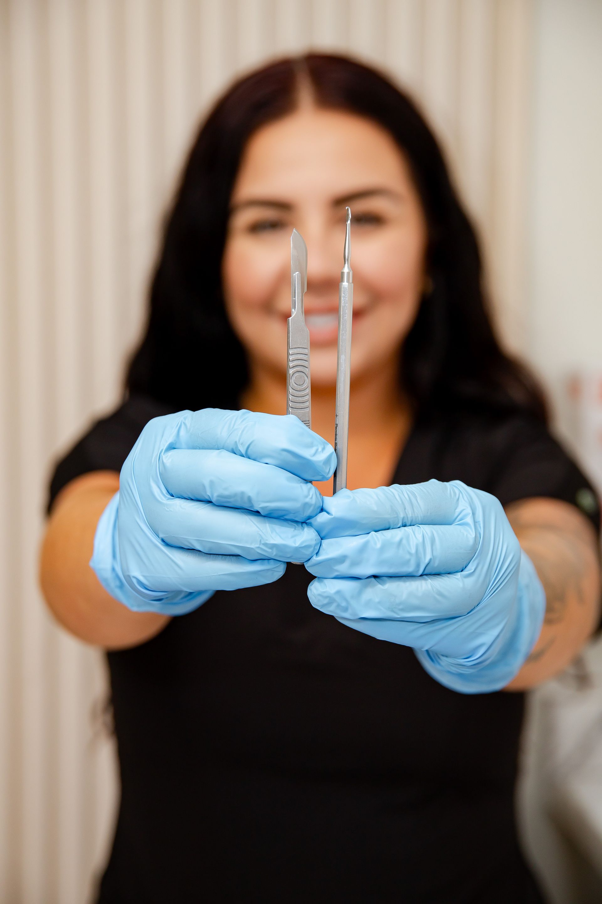 A woman wearing blue gloves is holding a pair of tweezers.