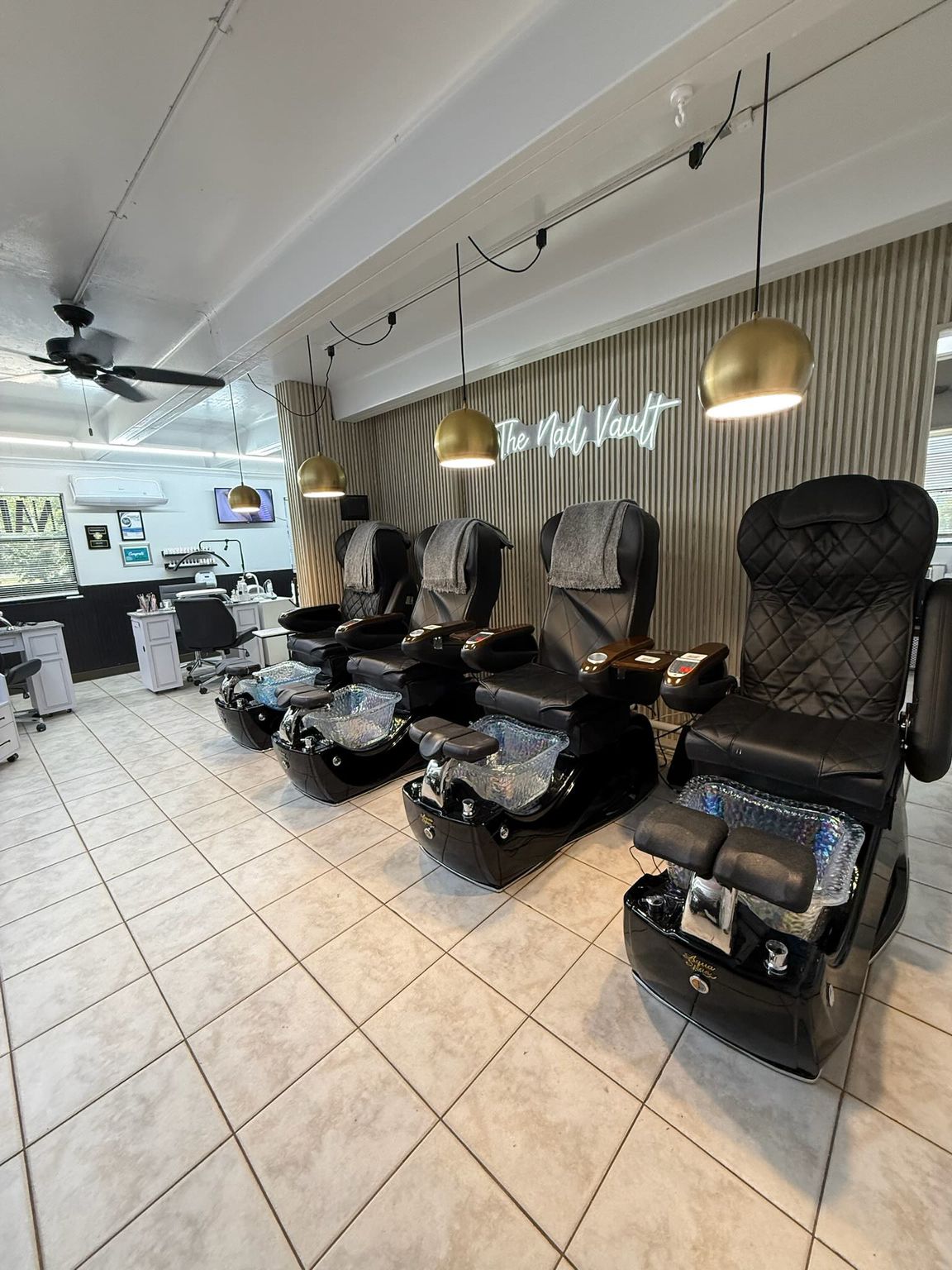 A row of black chairs are lined up in a nail salon.