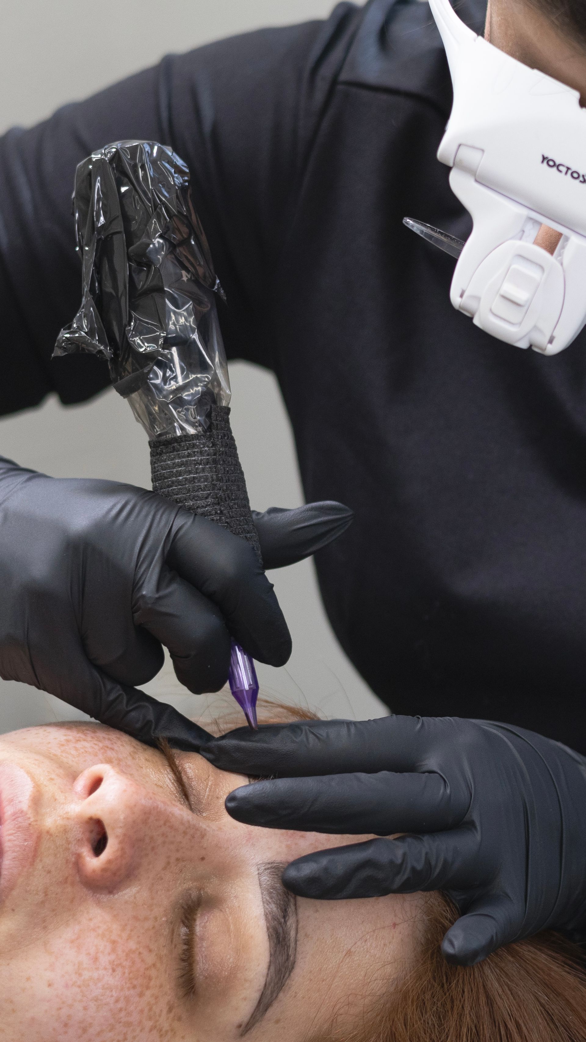 A woman is getting a tattoo on her eyebrows.