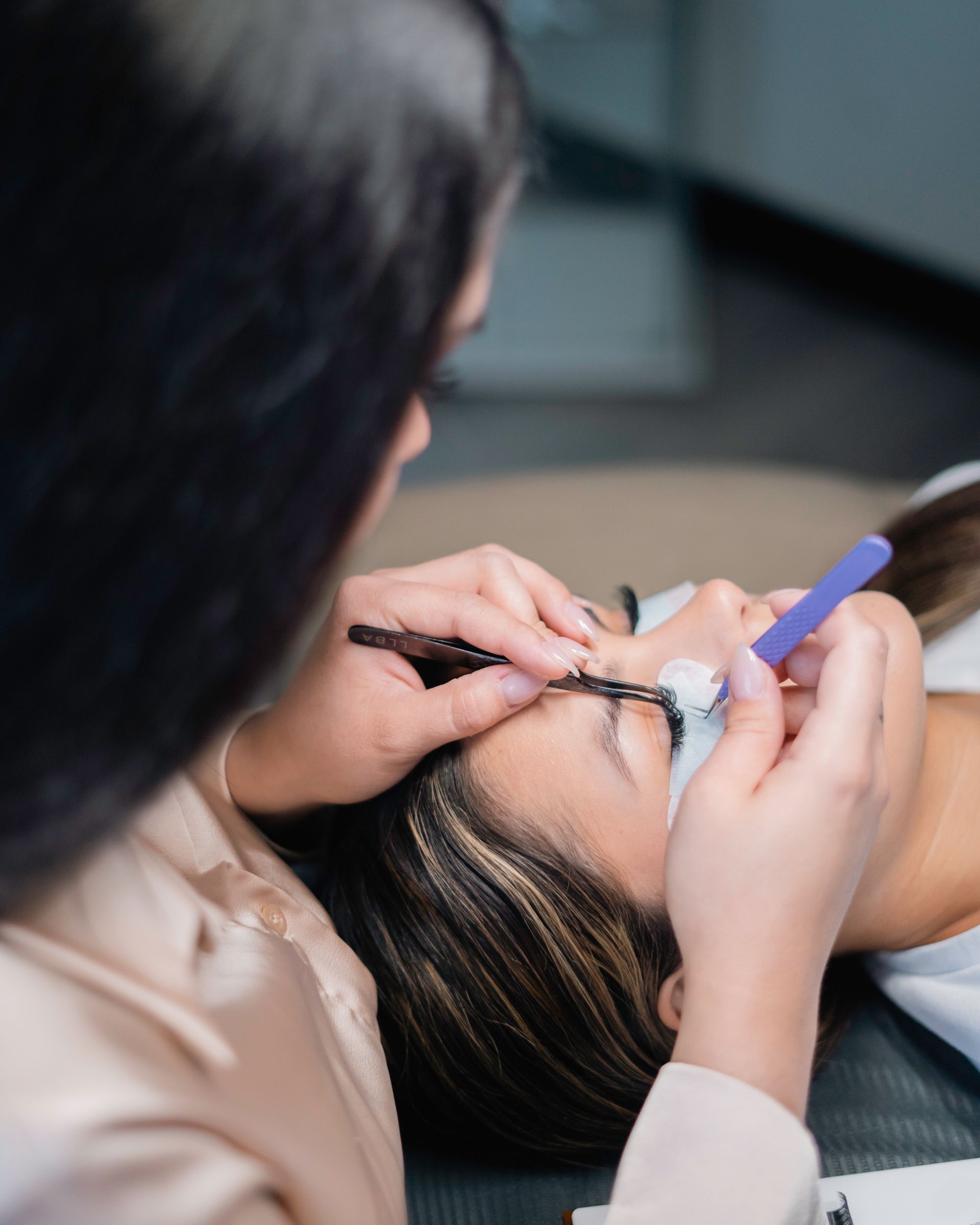 A woman is getting her eyelashes done by another woman