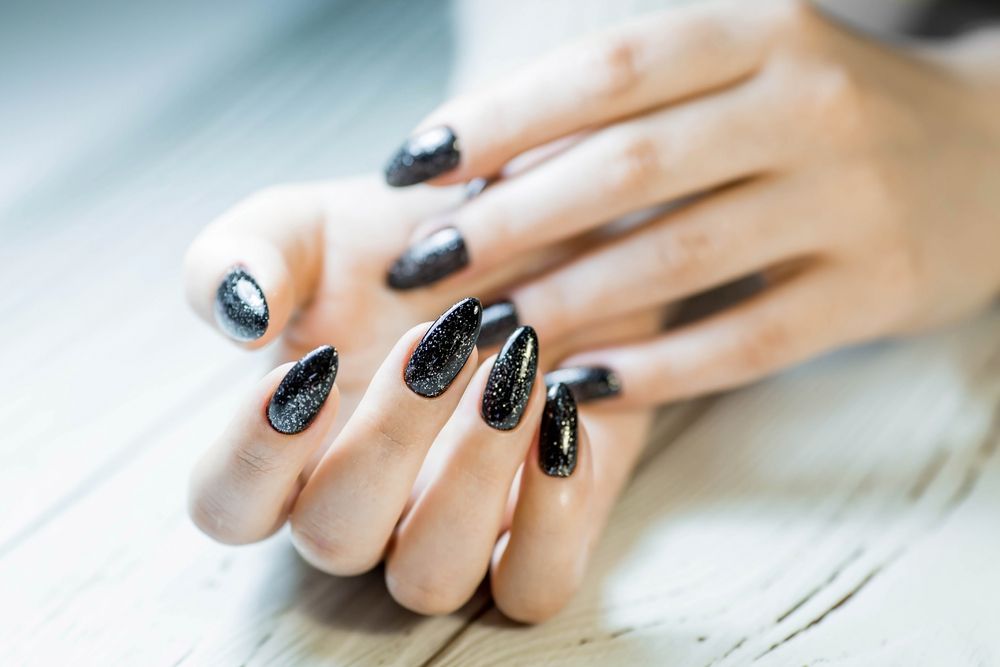 A close up of a woman 's hands with black nails on a wooden table.