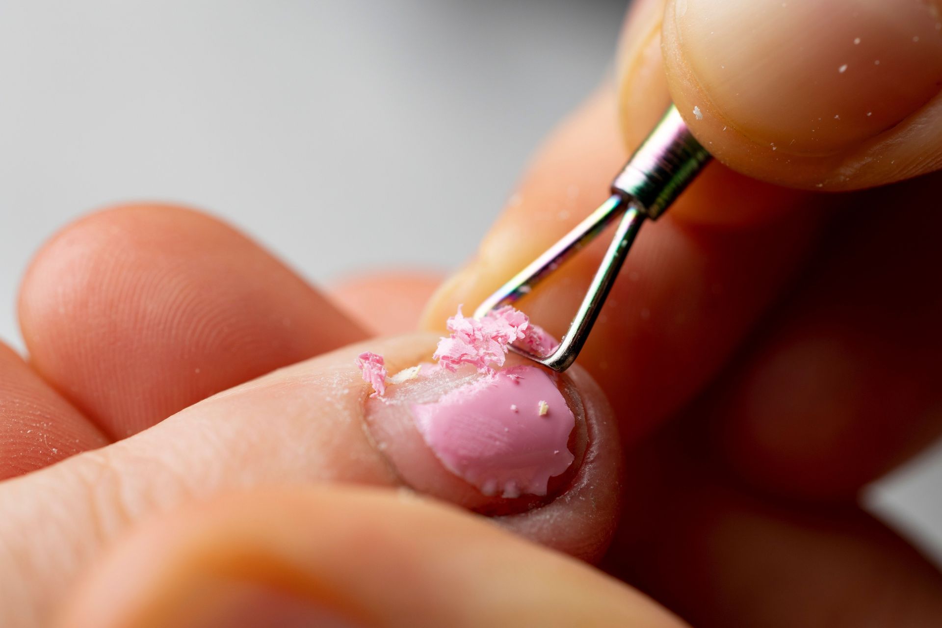 A person is removing pink nail polish from their nails with a tool.