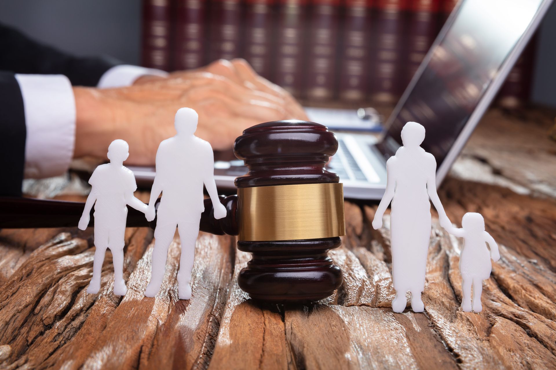 Toy people around a gavel on a wooden table, with a laptop and books in the background