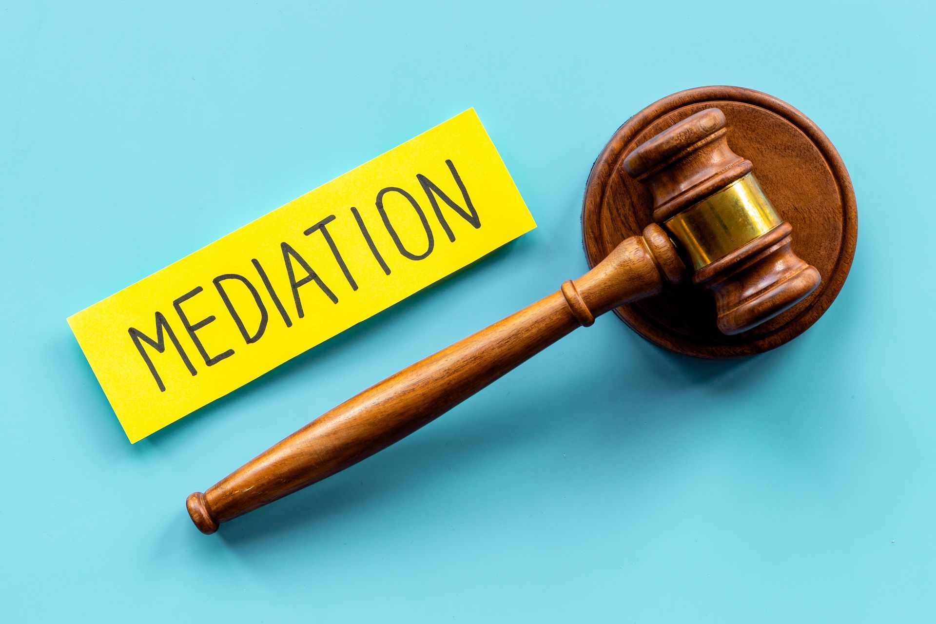 A wooden judge 's gavel and a yellow sticker with the word mediation written on it.